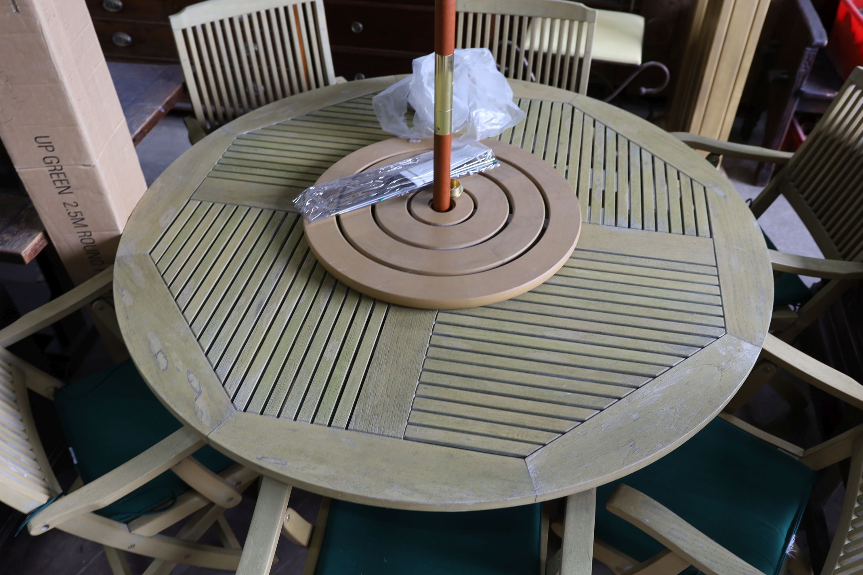 A teak garden set comprising circular table 148 cms diameter height 75 cms with 'Lazy Susan', parasol and waterproof cover and metal base, six folding elbow chairs and seat cushions.